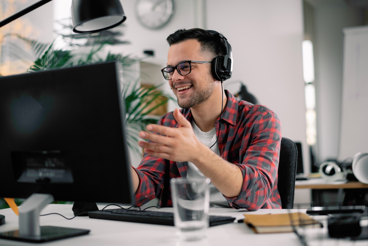 Junge Mann sitzt mit Kopfhörern vor einem Monitor.