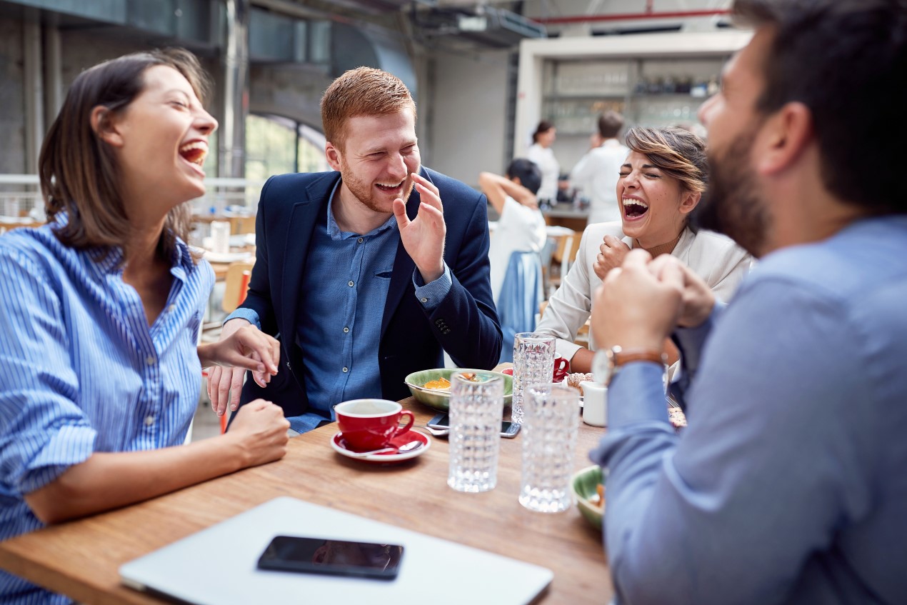 Gruppe Frauen und Männer sitzt in der Kantine und lacht.