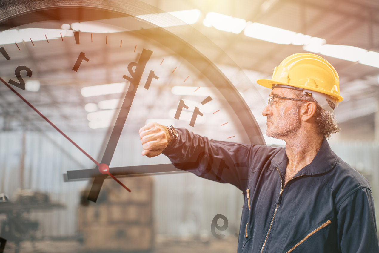 Arbeiter mit Schutzhelm schaut auf seine Armbanduhr..